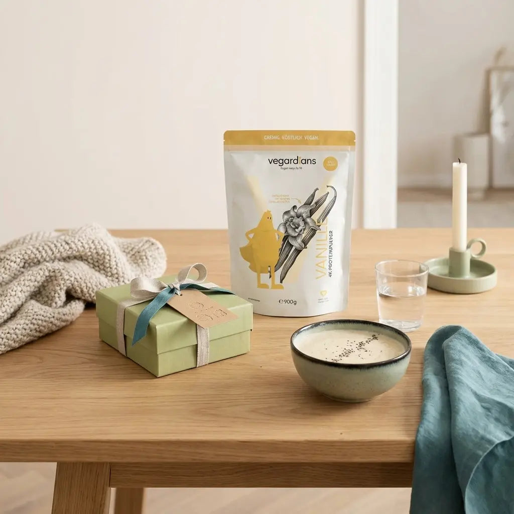 Wie lautet das dreiwortige Weihnachtszitat? Minimalistische Küchenaufnahme: Geschenkbox mit handgestempeltem Anhänger (nicht lesbar), Glas Wasser, veganer Shake im Morgenlicht